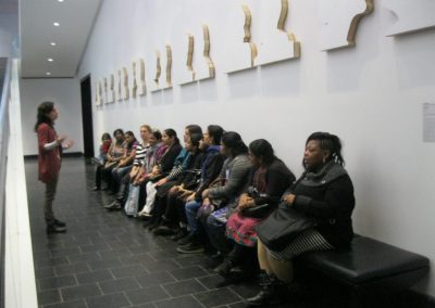 Une animatrice parle à un groupe de femmes assisent sur un banc au musée des beaux-arts