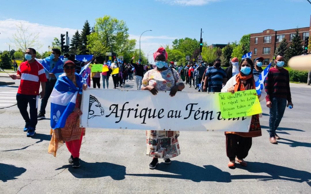 Les employées d'Afrique au Féminin tiennent une bannière avec le nom de l'organisme lors d'une manifestation pour la résidence permanente